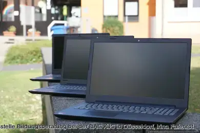 Drei Laptops liegen auf Steinsitzbänken in einer Grünanlage