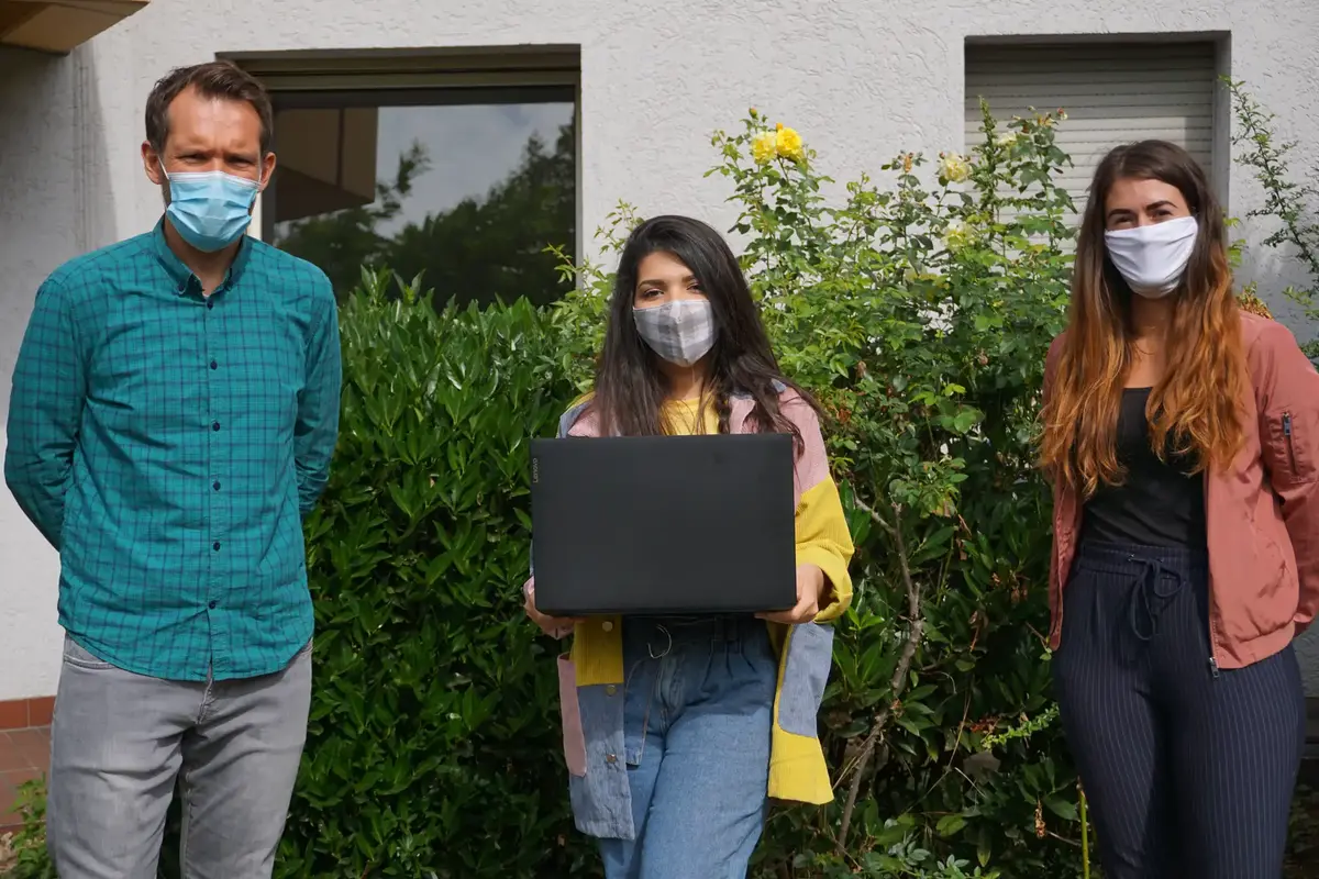 Jens Buschmeier, Ranim Kordy und Sandra Ape stehen vor einem Gebäude. Ranim hält einen Laptop in den Händen